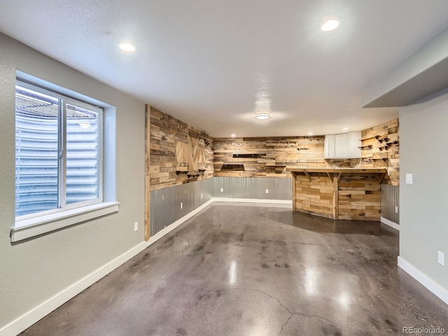 interior space featuring concrete flooring, recessed lighting, wooden walls, and baseboards