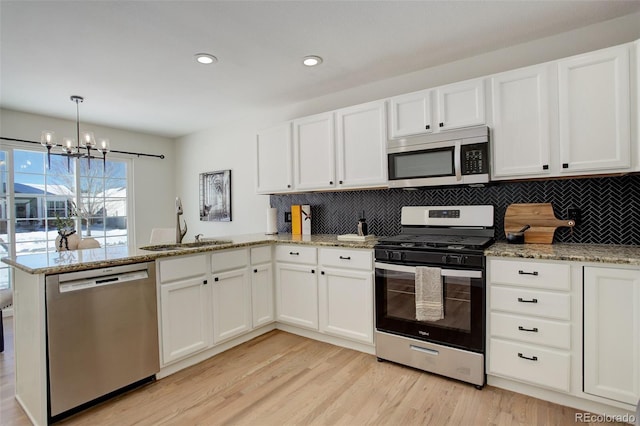 kitchen with white cabinetry, kitchen peninsula, stainless steel appliances, decorative light fixtures, and sink