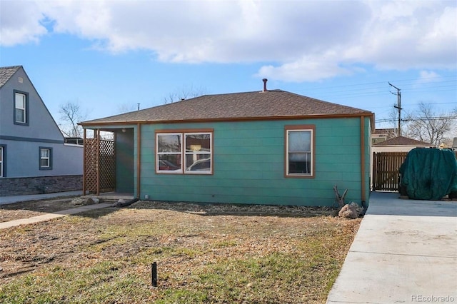 view of front of house featuring concrete driveway, fence, and roof with shingles