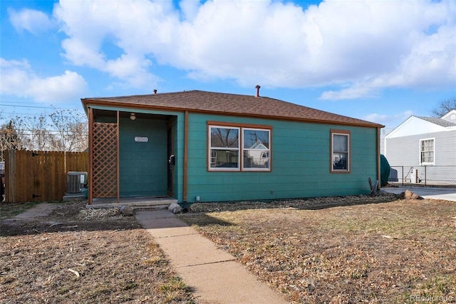 bungalow-style house with fence, central AC, and roof with shingles