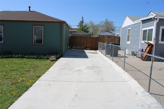 view of side of home featuring a lawn, roof with shingles, fence, and concrete driveway