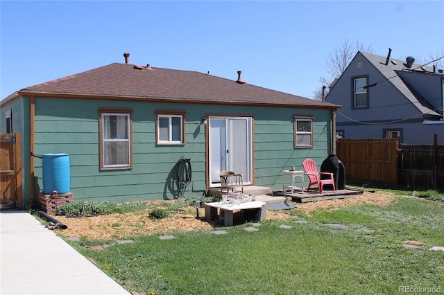 rear view of house featuring a lawn, roof with shingles, and fence