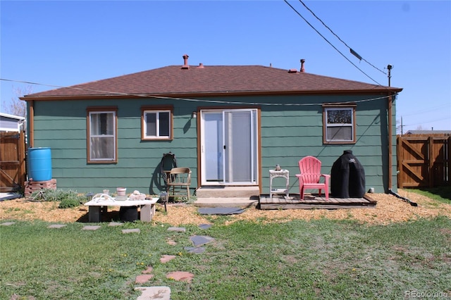 rear view of property with a shingled roof, fence, and a yard
