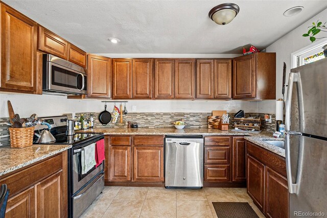 1730 W 51st Ave, Denver, CO 80221 - kitchen with appliances with stainless steel finishes, light stone counters, brown cabinets, and light tile patterned flooring