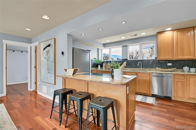 kitchen with light hardwood / wood-style floors, appliances with stainless steel finishes, a kitchen breakfast bar, sink, and a kitchen island