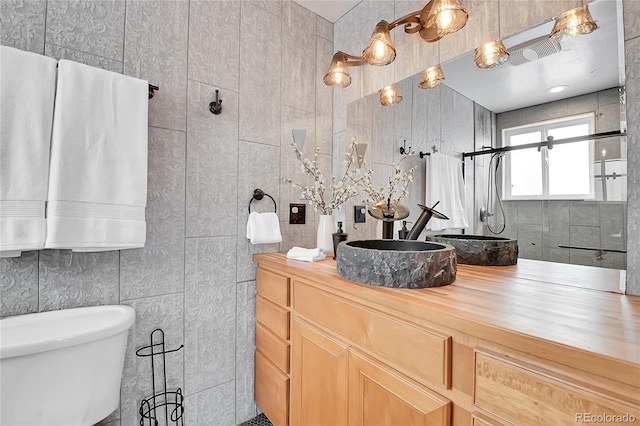 bathroom featuring walk in shower, toilet, vanity, and tile walls