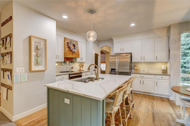 8229 Cottongrass Ct, Castle Pines, CO 80108 - kitchen featuring arched walkways, stainless steel appliances, white cabinets, light wood-type flooring, and decorative backsplash
