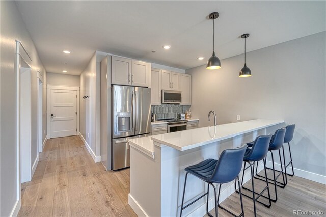 kitchen with tasteful backsplash, a breakfast bar, a peninsula, stainless steel appliances, and light wood-style floors