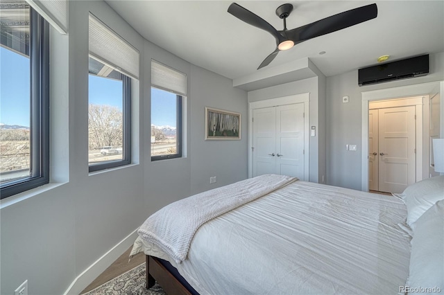 bedroom with ceiling fan, an AC wall unit, a closet, and baseboards