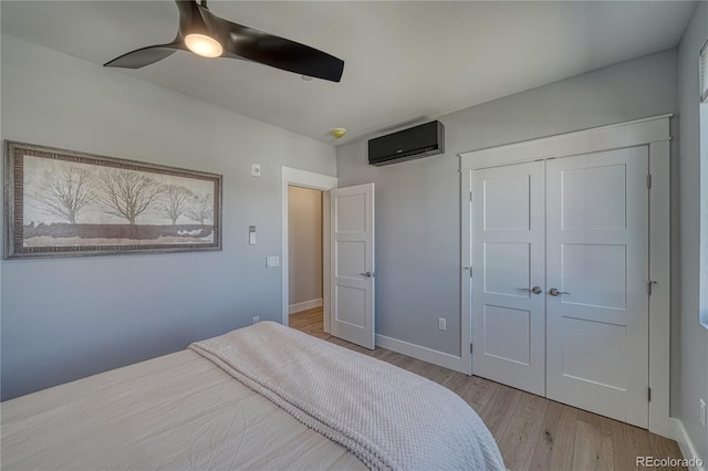 bedroom with a closet, an AC wall unit, ceiling fan, wood finished floors, and baseboards