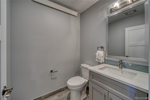 half bathroom featuring toilet, wood finished floors, vanity, visible vents, and baseboards