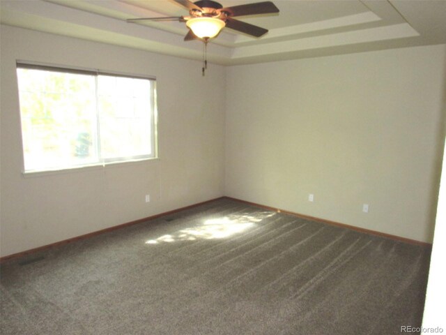 empty room with baseboards, carpet, ceiling fan, and a tray ceiling