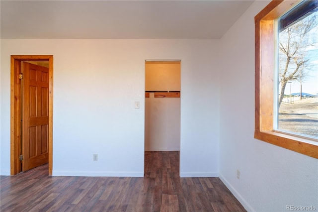 unfurnished bedroom featuring a walk in closet, dark wood-type flooring, and a closet