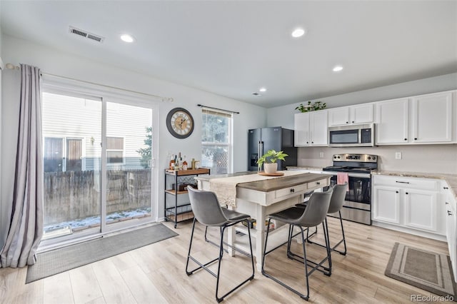 kitchen featuring white cabinets, light hardwood / wood-style floors, light stone counters, and stainless steel appliances