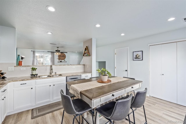 kitchen with white cabinetry, dishwasher, sink, ceiling fan, and light stone countertops