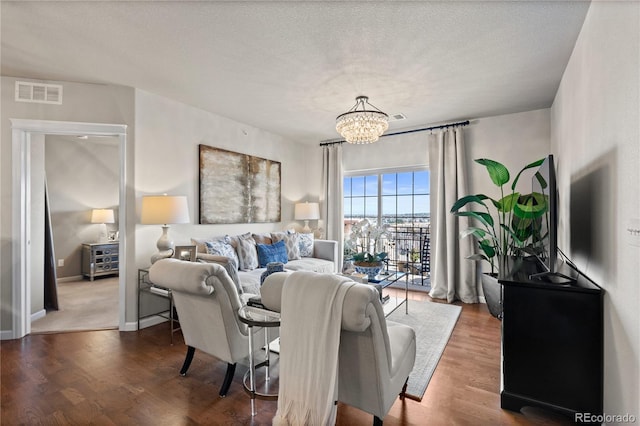 living room featuring a textured ceiling, wood finished floors, visible vents, and a chandelier