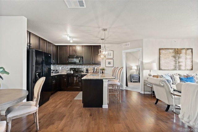 kitchen featuring visible vents, a sink, black appliances, a kitchen breakfast bar, and open floor plan