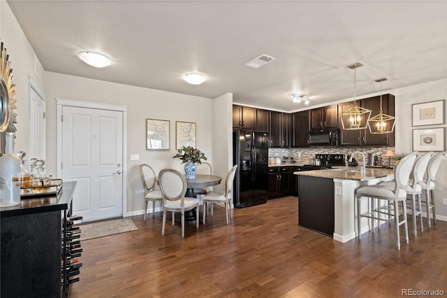 kitchen with visible vents, dark brown cabinetry, a kitchen bar, a peninsula, and black appliances