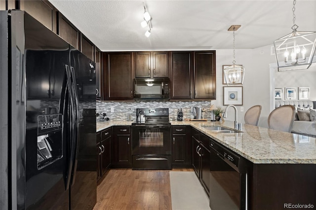 kitchen with light wood finished floors, a chandelier, a peninsula, black appliances, and a sink