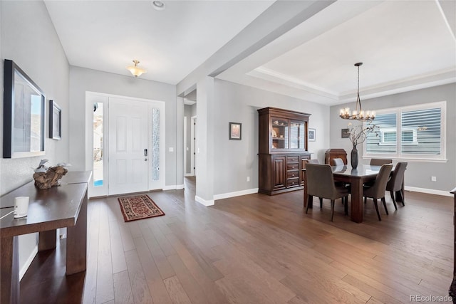 entryway with a tray ceiling, an inviting chandelier, and dark wood-type flooring