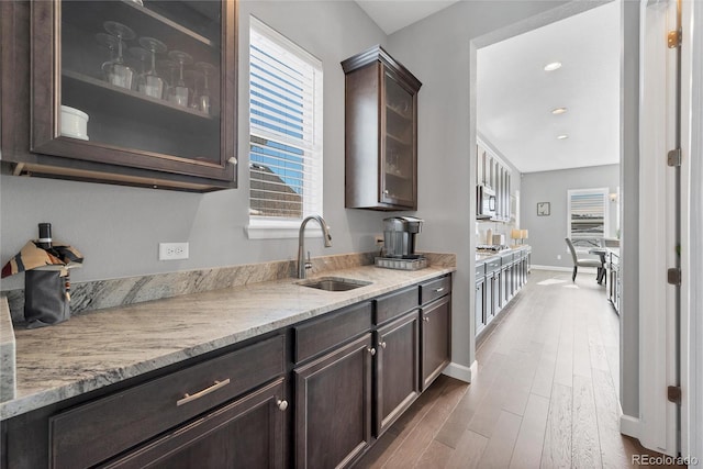 kitchen featuring sink, dark brown cabinets, dark hardwood / wood-style floors, and light stone counters