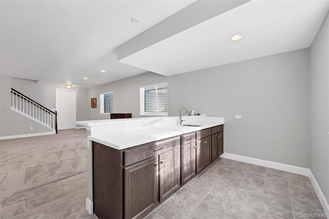 kitchen with light colored carpet, sink, dark brown cabinets, and kitchen peninsula