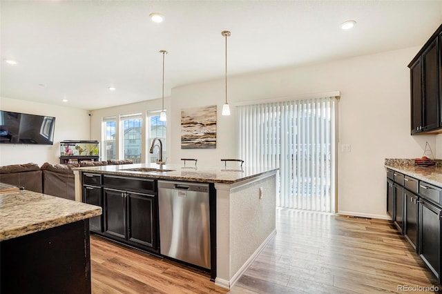 kitchen with light stone counters, light wood-style floors, a kitchen island with sink, a sink, and dishwasher