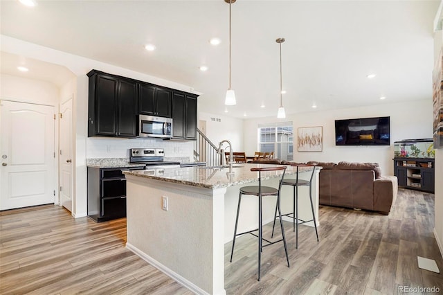 kitchen featuring stainless steel appliances, light wood-style floors, backsplash, and light stone counters