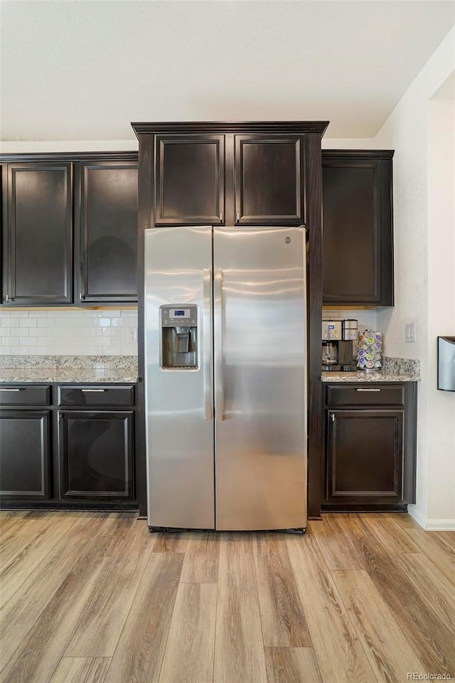 kitchen featuring light wood-style floors, dark brown cabinets, light stone countertops, tasteful backsplash, and stainless steel fridge