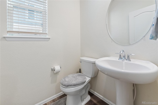 half bathroom with wood finished floors, toilet, and baseboards