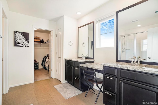 bathroom with double vanity, a stall shower, visible vents, a spacious closet, and a sink