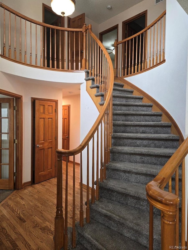 stairs featuring a textured ceiling, a towering ceiling, and hardwood / wood-style flooring