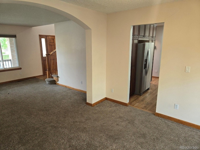 spare room featuring a textured ceiling and dark colored carpet