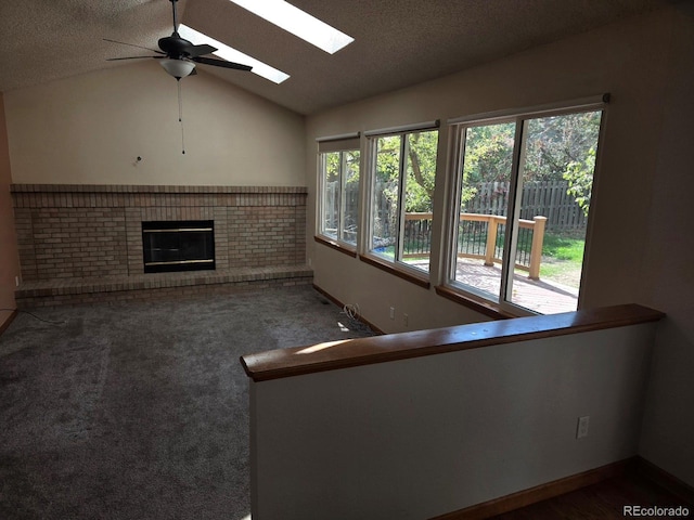 unfurnished living room with lofted ceiling with skylight, ceiling fan, a textured ceiling, a fireplace, and dark carpet