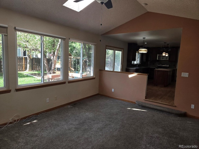 unfurnished living room with vaulted ceiling with skylight, plenty of natural light, and carpet floors