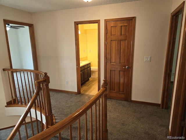 hallway with a textured ceiling and dark carpet