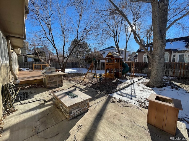 snow covered patio featuring a playground and a wooden deck