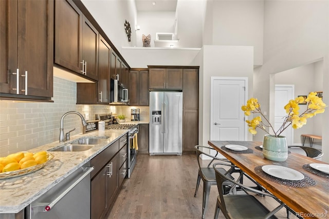 kitchen featuring light stone counters, sink, hardwood / wood-style flooring, appliances with stainless steel finishes, and a towering ceiling