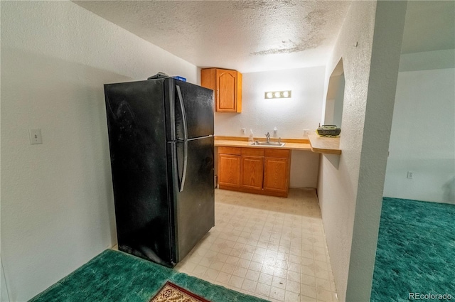 kitchen with a sink, a textured ceiling, freestanding refrigerator, light countertops, and a textured wall