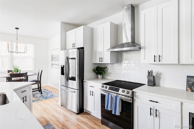 kitchen featuring white cabinetry, hanging light fixtures, light hardwood / wood-style floors, stainless steel appliances, and wall chimney range hood