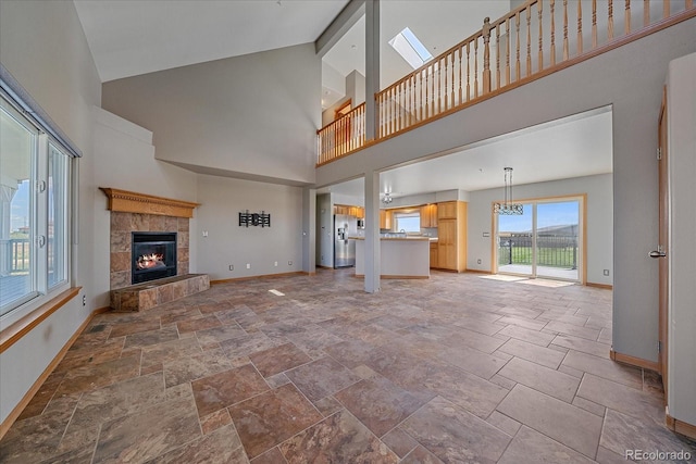 32800 E 137th Way, Brighton, CO 80603 - unfurnished living room with high vaulted ceiling, a tiled fireplace, baseboards, stone tile floors, and a chandelier