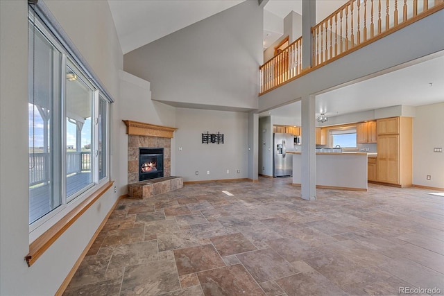 32800 E 137th Way, Brighton, CO 80603 - unfurnished living room featuring light stone finish floors, baseboards, a towering ceiling, and a fireplace