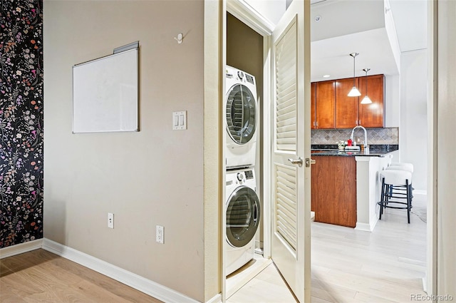 laundry area featuring stacked washer / drying machine, light wood-style flooring, baseboards, and a sink
