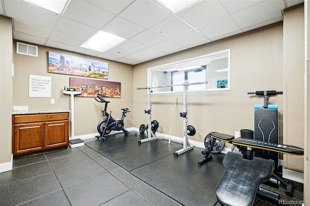 exercise room with baseboards and a paneled ceiling