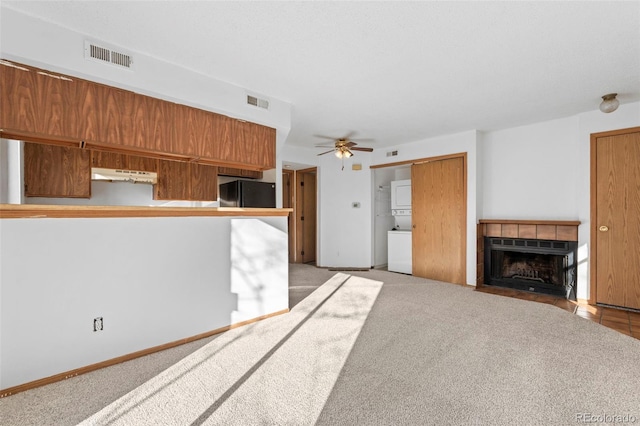 8701 Huron St Unit 5-210, Thornton, CO 80260 - kitchen featuring estacked washer and dryer, under cabinet range hood, freestanding refrigerator, a fireplace, and light colored carpet