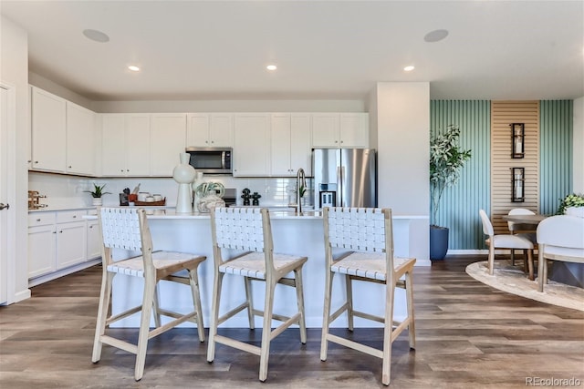 kitchen featuring backsplash, dark wood-type flooring, a breakfast bar, an island with sink, and stainless steel appliances