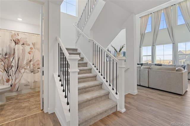 stairs featuring recessed lighting, baseboards, a towering ceiling, and wood finished floors