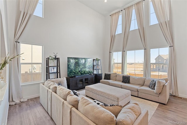 living area with light wood-type flooring, plenty of natural light, and a towering ceiling