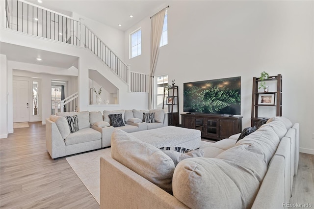 living room featuring stairway, baseboards, a high ceiling, recessed lighting, and light wood-style floors