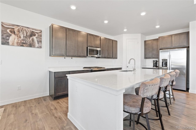 kitchen featuring a breakfast bar area, light wood finished floors, a sink, dark brown cabinets, and appliances with stainless steel finishes